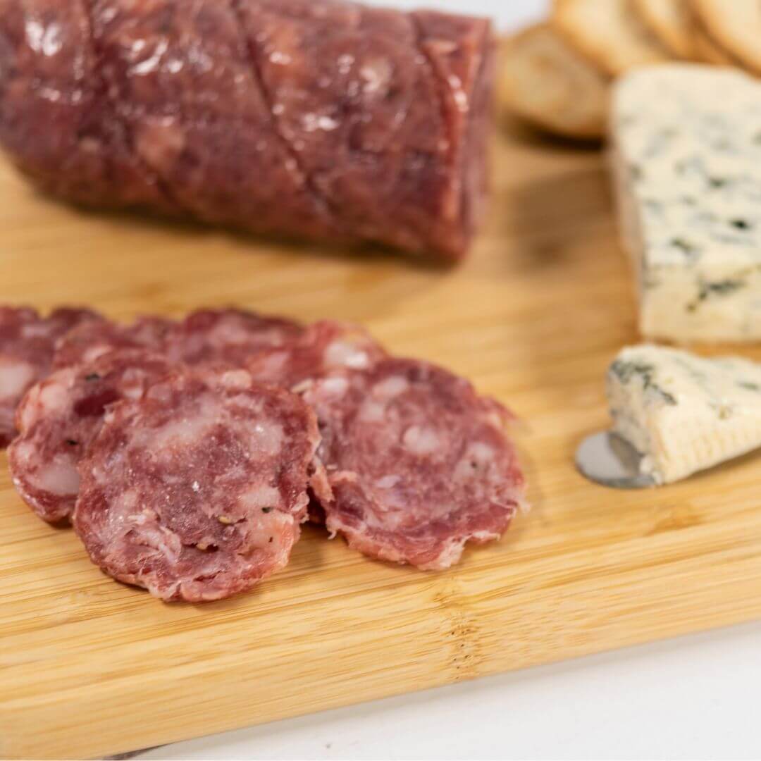 Danish Blue Salami thinly sliced on a wooden board, placed next to blue vain cheese