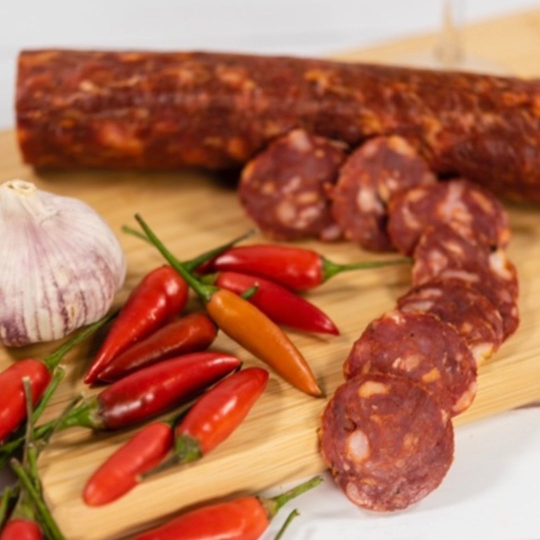 Pepperoni Salami thinly sliced on a wooden board with a pile of chilli's and garlic next to it