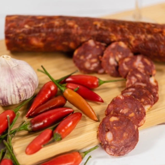 Pepperoni Salami thinly sliced on a wooden board with a pile of chilli's and garlic next to it