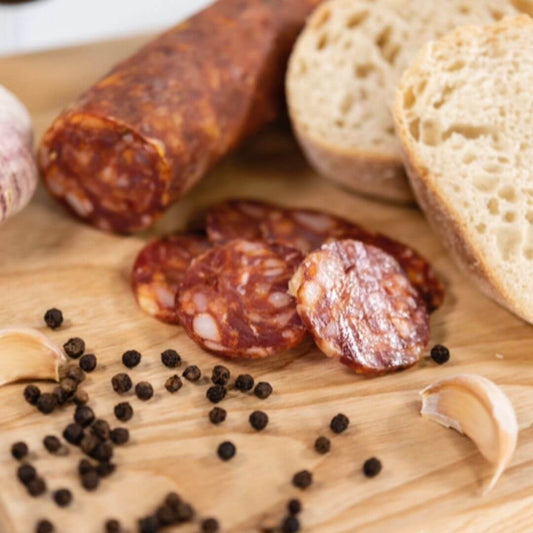 Cacciatore Mild Salami on a wooden board with sourdough bread and peppercorns