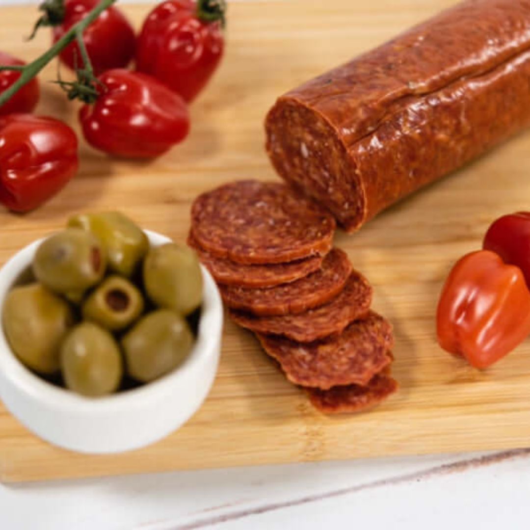 Mild Chilli Hungarian Salami thinly sliced on a wooden board, surrounded by cherry tomatoes on the wine and a bowl of green stuffed olives