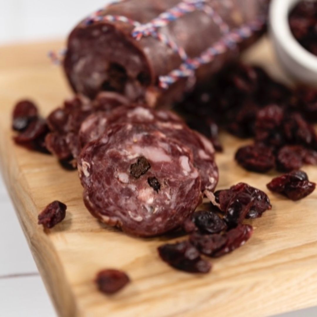 Venison salami thinly sliced on a wooden board surrounded by cranberries