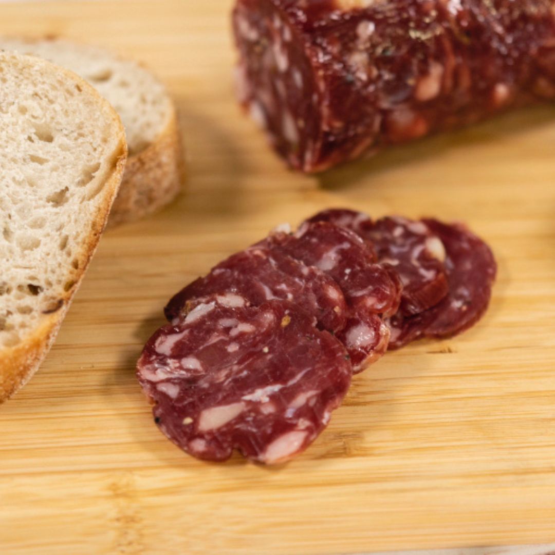 Wild Boar Salami thinly sliced on a wooden board, paired with 2 slices of bread